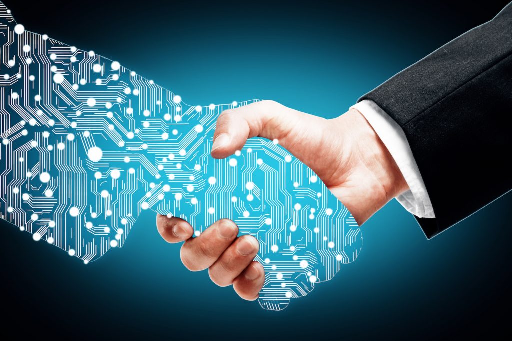 A human hand in a suit shakes hands with a digital hand made of circuitry, symbolizing the partnership between people and technology—an ideal representation of Co-Managed IT Services—set against a blue glowing background.
